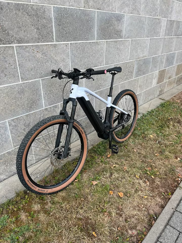 CUBE Reaction Hybrid SLT 750 29 E-MTB Hardtail 2022, weiß-schwarz, Größe L, mit braunen Reifen, vor Ziegelwand.