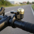 Procraft Race Bell Mini: goldene, superleichte Rennrad-Fahrradklingel auf schwarzem Carbon-Lenker.