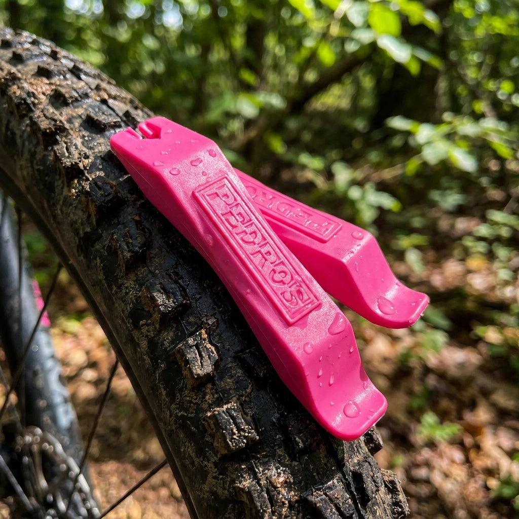 Pedros pinke 2-teilige Reifenheber mit Wassertropfen liegen auf einem matschigen Fahrradreifen in der Natur.