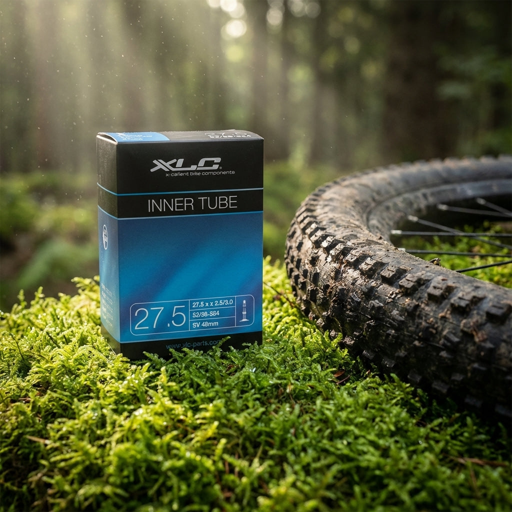 XLC Fahrradschlauch 27.5 x 2.5/3.0 62/76-584 SV 48mm auf Moos neben Mountainbike-Reifen im Wald.