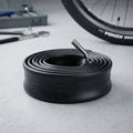 Kenda Fahrradschlauch Reha 10x2 (54-152) AV 45/45° Ventil auf Betonboden, im Hintergrund Fahrradreifen & Werkzeug.