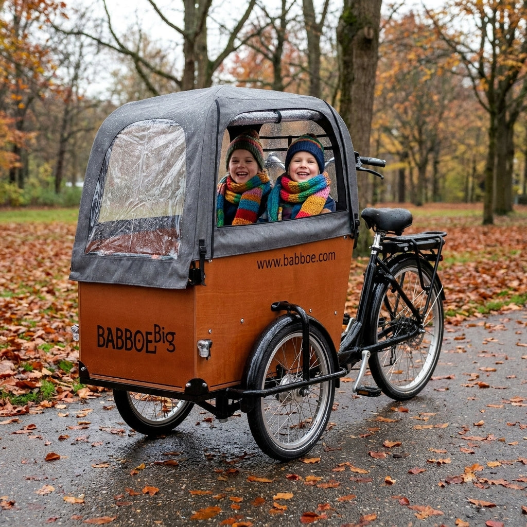 Regenverdeck Babboe Big grau mit lachenden Kindern im Lastenrad auf nassem Herbstweg.