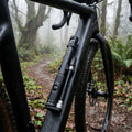 Crankbrothers Klic HP Handpumpe Midnight schwarz mit Rahmenhalter am nassen Fahrrad im nebligen Wald.