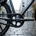 Schwarzer Hebie Chainglider Kettenschutz am nassen Fahrrad auf Kopfsteinpflaster.