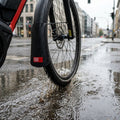 Schwarzer FAHRER Spritzlappen Latz am E-Bike Vorderrad spritzt Wasser in Pfütze.