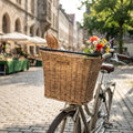 Basil Bremen Lenkerkorb Rattan-Look vorne am Fahrrad mit Baguette und bunten Blumen auf Kopfsteinpflaster.
