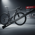 DT SWISS Aerolite Messerspeiche in Schwarz vor einem unscharfen Rennrad und einer Anzeigetafel.