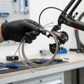 Hand hält Campagnolo Schaltzüge 1,2mm Niro 2000mm neben Rennrad-Schaltwerk. Fahrradreparatur.