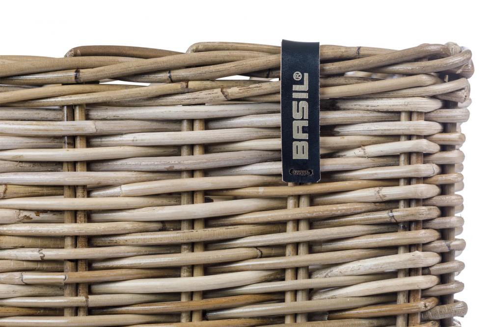 Detailansicht des handgeflochtenen Basil Dax L Vorderradkorbs aus grauem Rattan mit schwarzem Basil-Logo-Label.