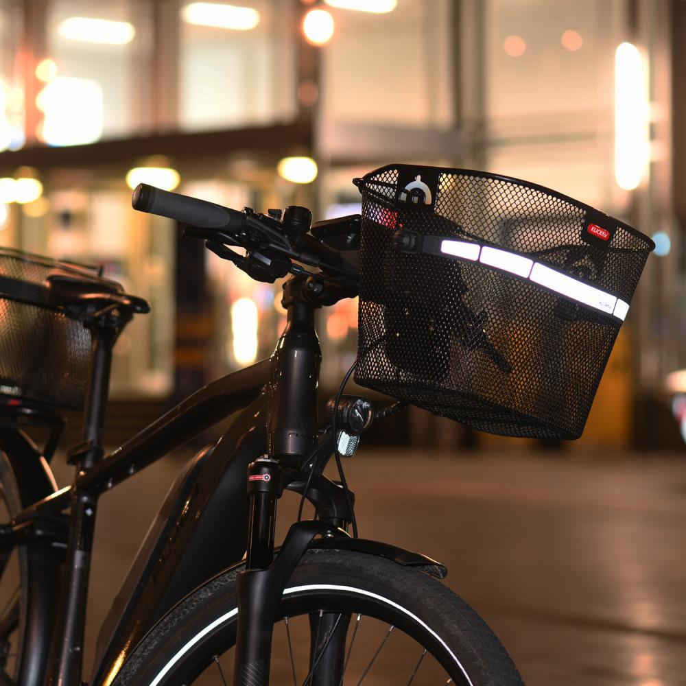 Schwarzer KLICKfix Uni Lenkerkorb 16L, feinmaschig mit Reflektor, montiert an einem Fahrradlenker bei Nacht.
