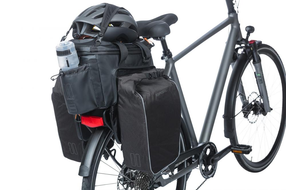Schwarze Basil Miles Tarpaulin XL Pro MIK 2.0 Gepäckträgertasche am grauen Fahrrad, mit Helm und Trinkflasche.