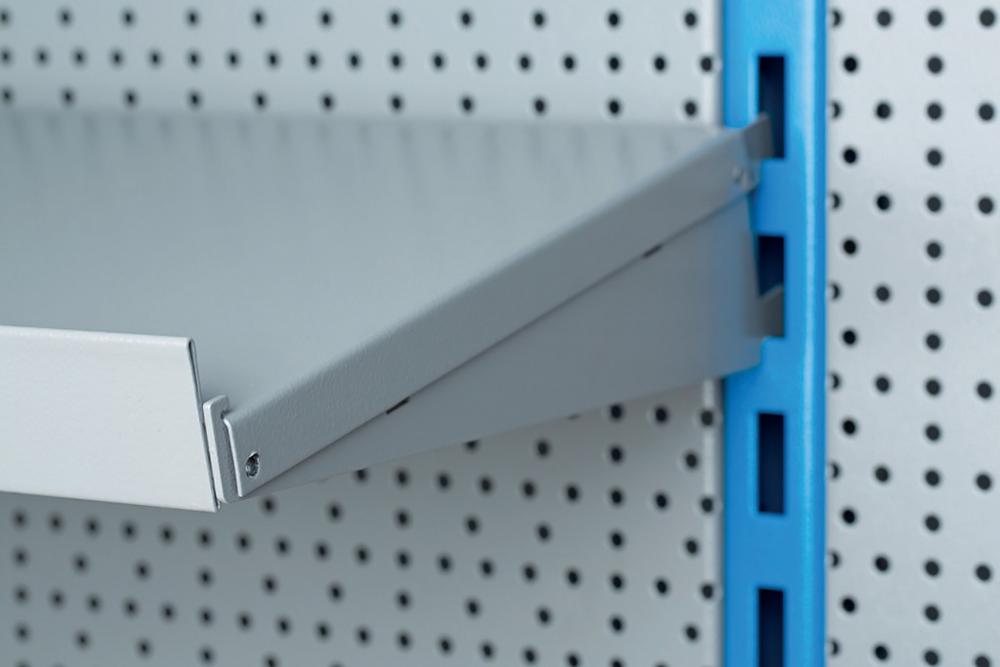 Grauer Fachboden Unior 990SHELF mit Fachbodenträger, montiert an blauem Regalprofil vor Lochwand.