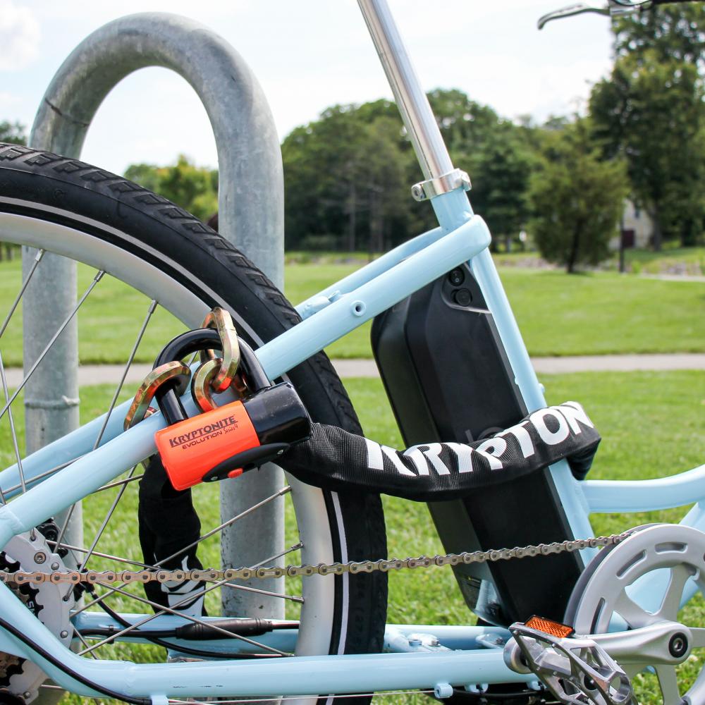 Kryptonite New York Chain 1217 Kettenschloss mit Evolution 14mm Disc Lock sichert hellblaues E-Bike am Ständer.