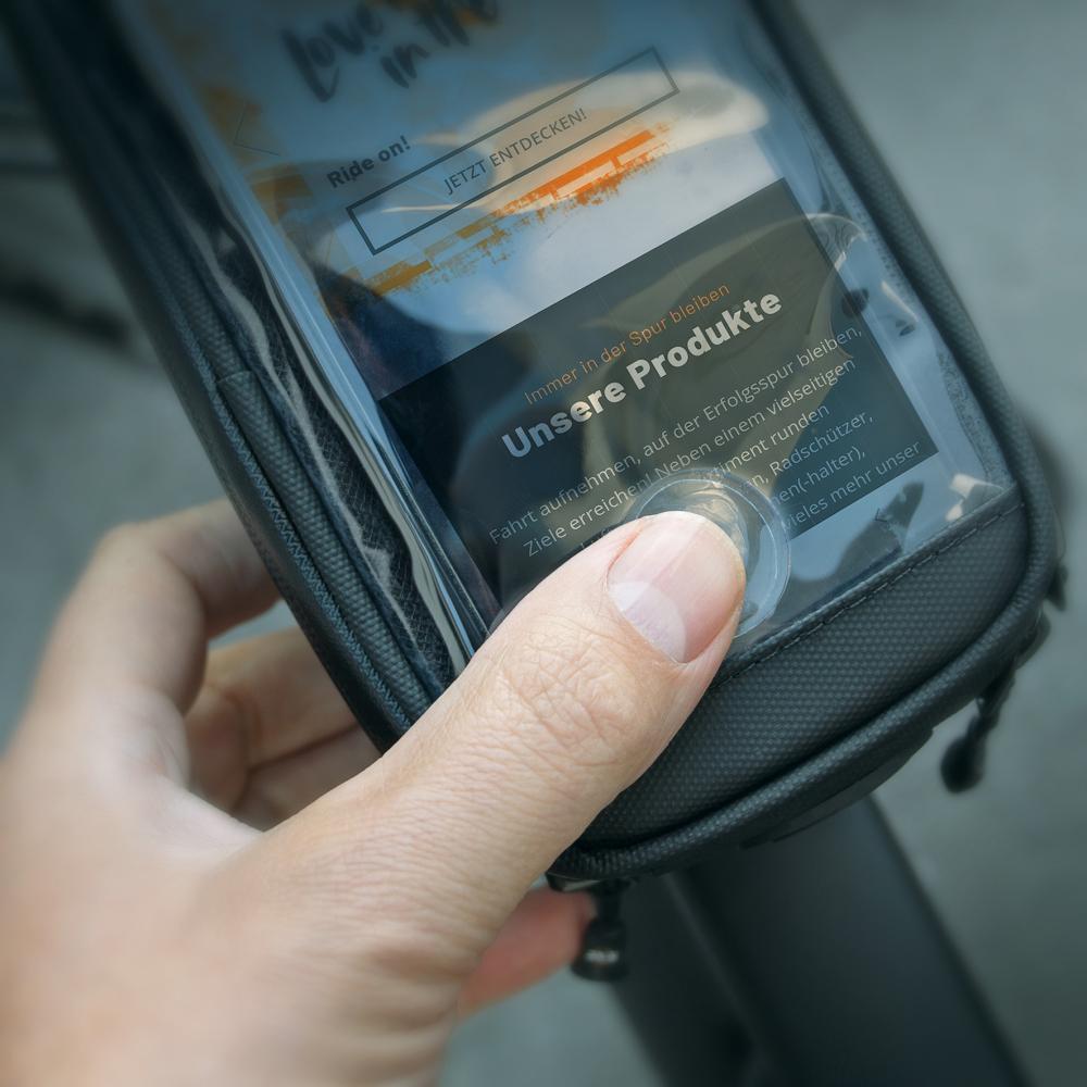 Schwarze SKS Explorer Smart Oberrohrtasche mit bedientem Smartphone, ideal für Bikepacking und Touren.
