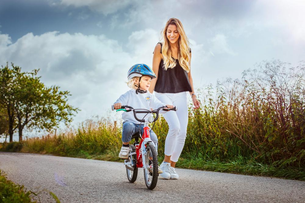 Kind auf rotem Fahrrad mit Schwalbe Little Joe 16 Zoll Kinderfahrradreifen Drahtreifen mit Reflex, Mutter läuft.