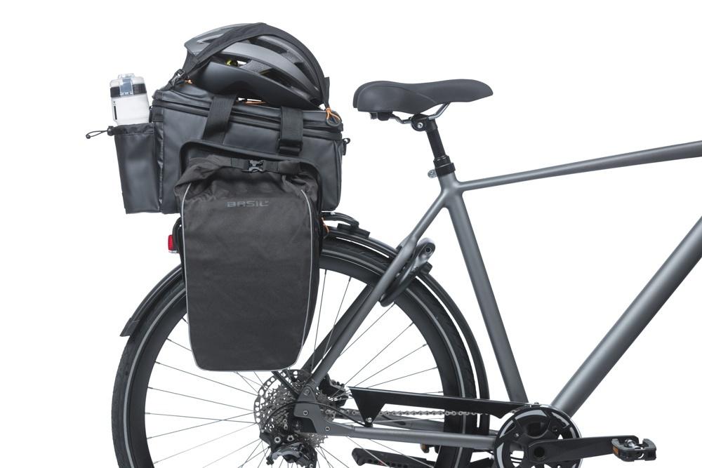 Basil Gepäckträgertasche Miles Tarpaulin XL Pro MIK 2.0 schwarz am Fahrrad mit Helm und Trinkflasche.