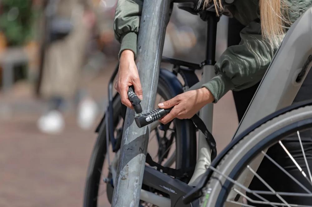 Frau sichert Fahrrad mit AXA Kettenschloss Absolute C5-90 Code 90 Zahlencode an Poller.