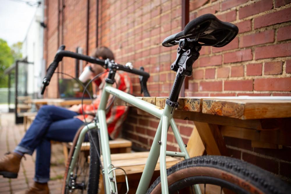 Cane Creek Thudbuster G4 ST Sattelstütze schwarz mit Parallelogramm-Mechanik am Fahrrad vor Ziegelwand.