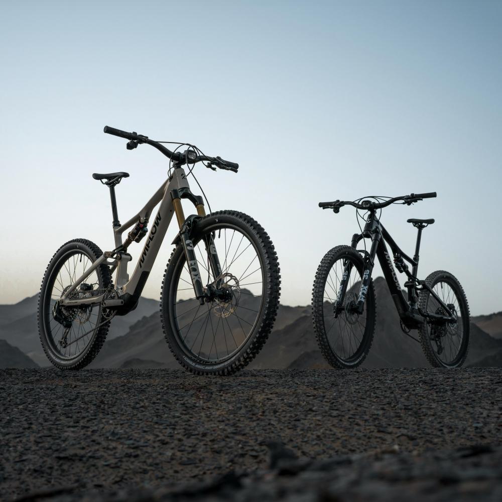 Amflow PX Carbon E-Mountainbike Fully, beige und schwarz, auf Schotterpiste in bergiger Landschaft.