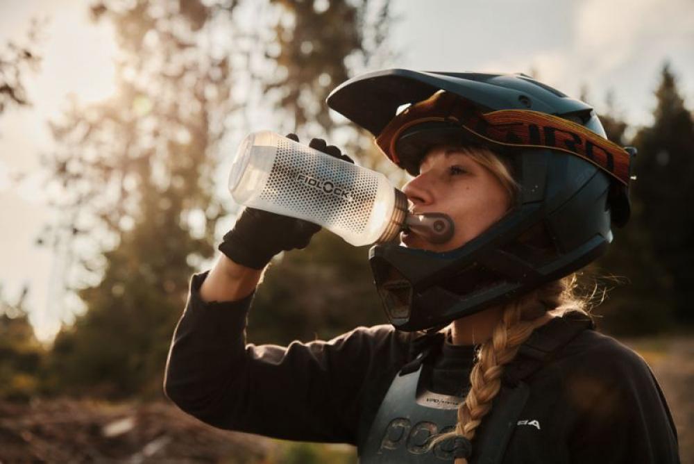 Mountainbikerin trinkt aus FIDLOCK TWIST 750ml Compact Trinkflasche mit magnetischem Halter.