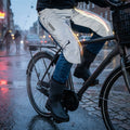 Rainlegs Arctic Beinschützer grau reflektierend an Radfahrer auf nassem Kopfsteinpflaster mit Lichtreflexen.