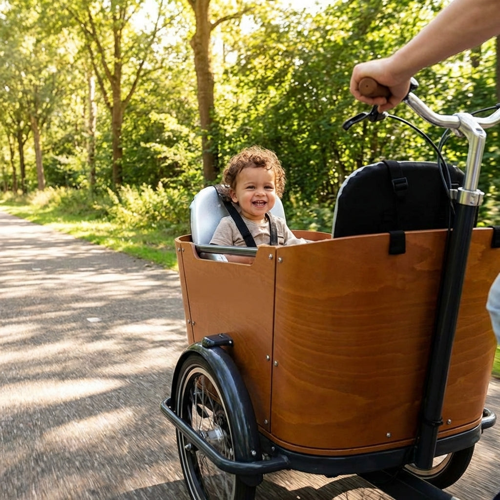 Babboe Sunny Silver Kindersitz: Lachendes Kind im Lastenrad auf grünem Waldweg.
