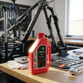 Rote RockShox Federungsöl 10 WT 1 Liter Flasche in einer Fahrradwerkstatt mit Fahrrad und Werkzeugen.