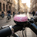 XLC Fahrradklingel Mingun DD-M09 Stripes Ø83mm berry weiß am Fahrradlenker, belebte Stadt im Hintergrund.
