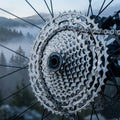 SHIMANO DEORE CS-M5100 11-fach 11-51 Kassette am Mountainbike-Hinterrad mit Kette, neblige Berge im Hintergrund.