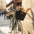 Basil Vorderradkorb Darcy L Rattan schwarz am grünen Fahrrad, mit bunten Blumen und Baguette, auf Pariser Kopfsteinpflaster.