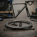 SRAM Schalt-/Bremskabel-Kit SlickWire Standard 5mm schwarz auf Holztisch vor Fahrradrahmen.