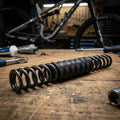 SR-Suntour harte Spiralfeder für SF18 XCR34-LOR auf Werkbank mit Fahrrad und Werkzeug im Hintergrund.
