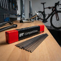 DT SWISS Competition J-Bend Speichen, schwarz, 100 Stück im Karton und lose auf Werkbank einer Fahrradwerkstatt.