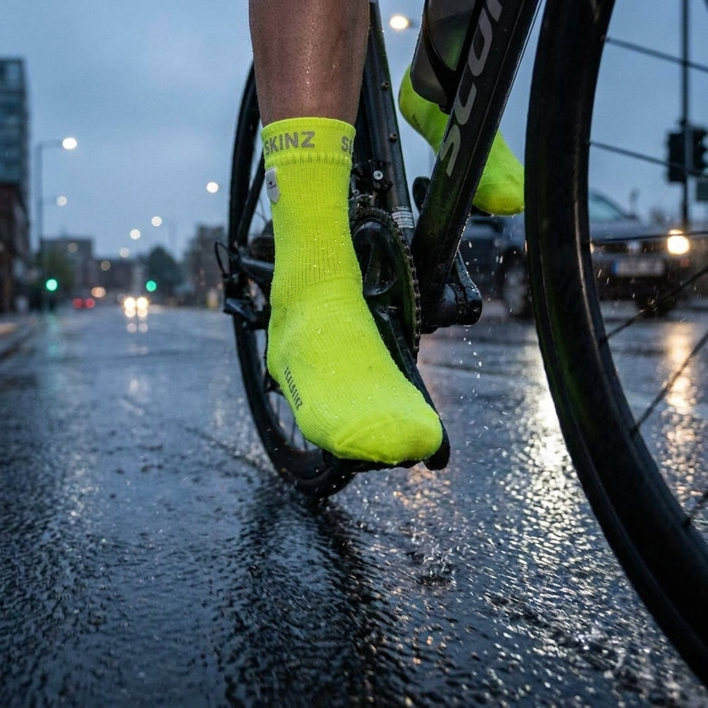 SealSkinz Thetford neon gelbe Überziehsocken an einem Radfahrer auf regennasser Straße, spritzt Wasser.