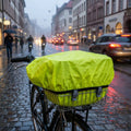 Neongelbe Racktime YOSHI Regenhülle auf Fahrradkorb mit Regentropfen in regnerischer Stadt.