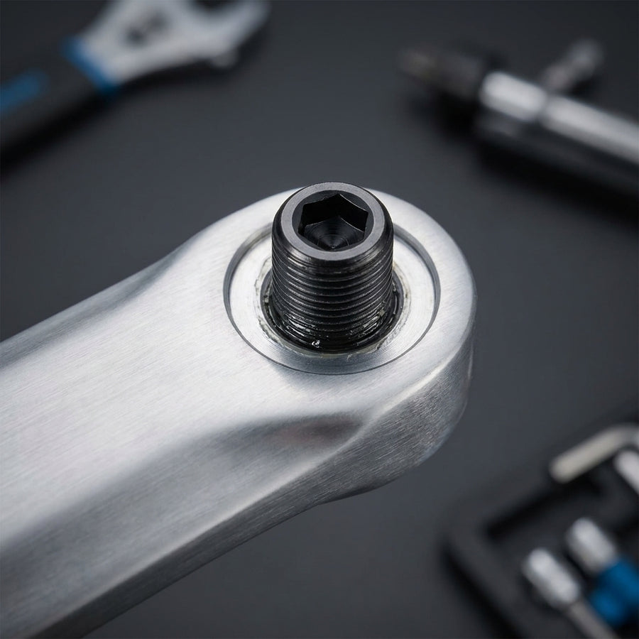 SHIMANO Klemmschraube M6x19 FC-M617 in silberner Fahrradkurbel, Nahaufnahme mit Werkzeug im Hintergrund.