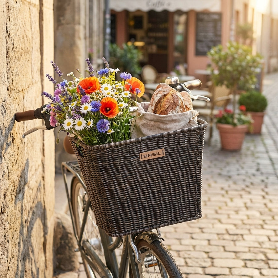 Basil Vorderradkorb Bremen FM aus dunkelbraunem Rattan am Fahrrad mit Blumen und Brot.
