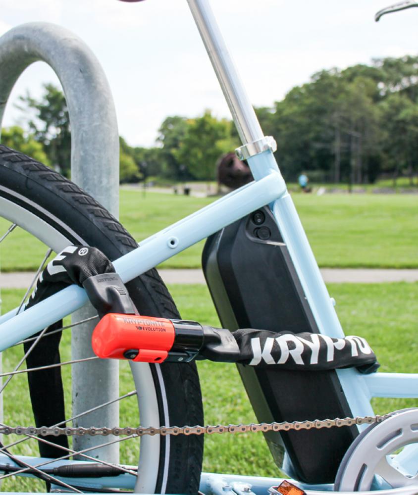 Kryptonite Evolution 1012 Kettenschloss in Schwarz und Orange sichert hellblaues E-Bike am Fahrradständer.