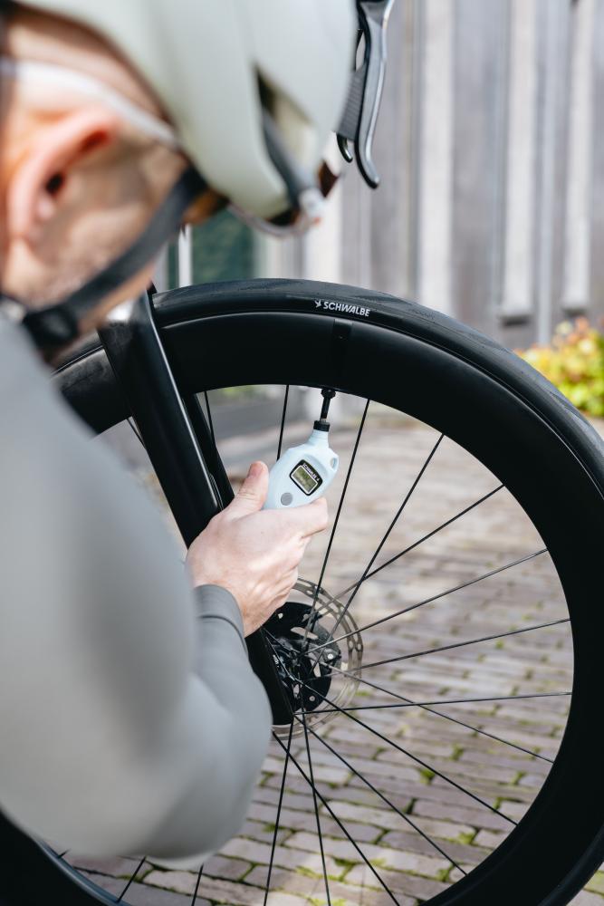 Nahaufnahme: Radfahrer misst Fahrradreifen-Luftdruck mit Schwalbe AIRMAX Pro digitalem Luftdruckmessgerät.