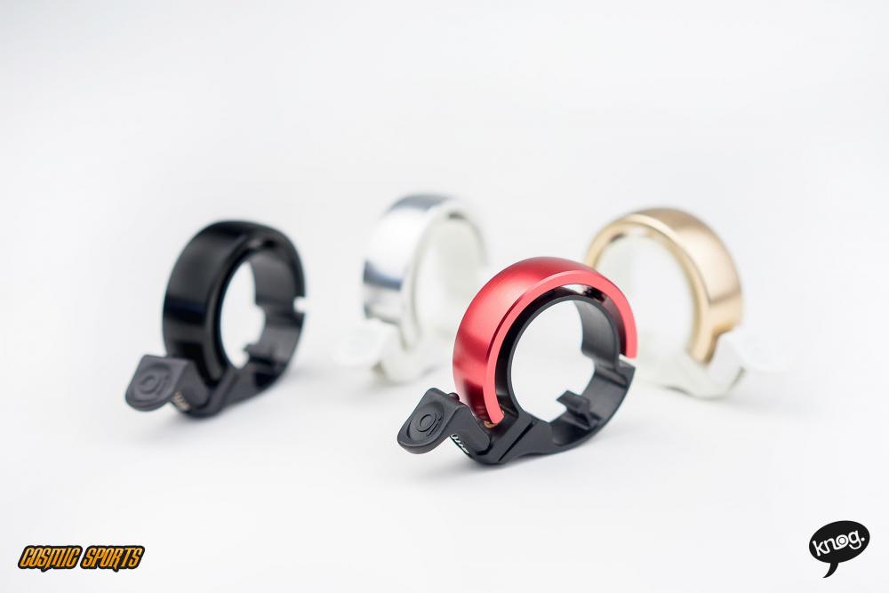 Knog Oi Classic Fahrradklingeln in Rot, Schwarz, Silber und Gold auf weißem Hintergrund.