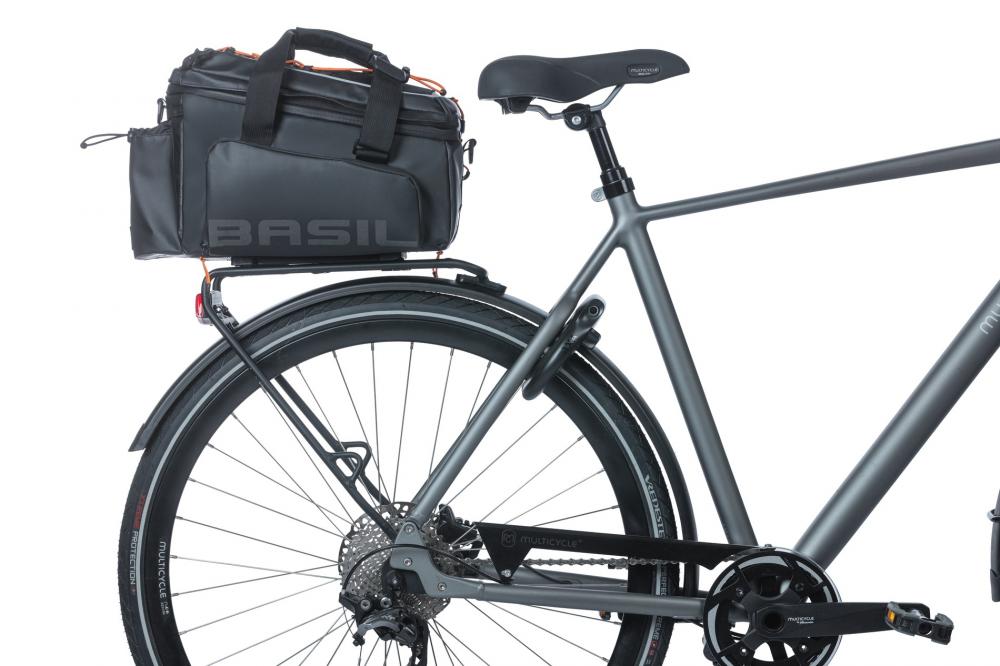 Basil Gepäckträgertasche Miles Tarpaulin XL Pro MIK 2.0 in Schwarz-Orange auf dem Gepäckträger eines grauen Fahrrads.