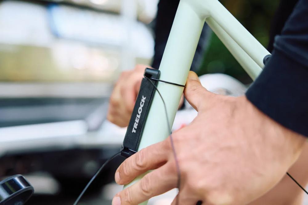 Person montiert TRELOCK ADD IT Fahrradhalterung flexibel an hellgrünem Rahmen für Schlösser & Flaschen.