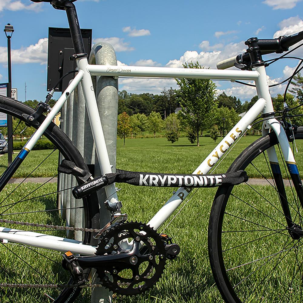 Kryptonite Keeper 712 Kettenschloss 120 cm schwarz sichert weißes Fahrrad an einer Stange vor Diebstahl.