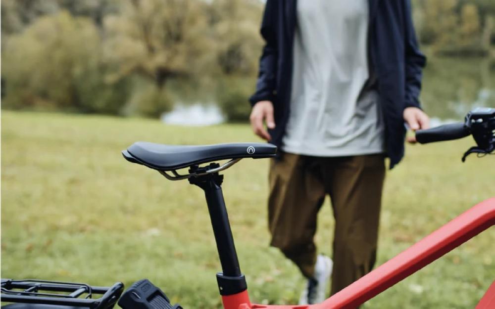 Schwarzer Selle Royal On Open Athletic Unisex Sattel auf rotem Fahrrad in Natur mit Person im Hintergrund.