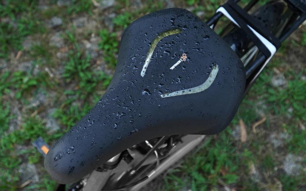 Selle Royal Lookin Evo Moderate Fahrradsattel, schwarz, nass mit Regentropfen auf der Oberfläche, vor Grün.