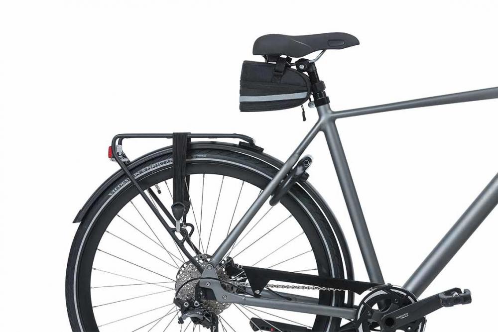 Basil Mada Satteltasche schwarz (1l) am grauen Fahrradsattel, mit Reflektorstreifen. Hinterrad, Gepäckträger sichtbar.