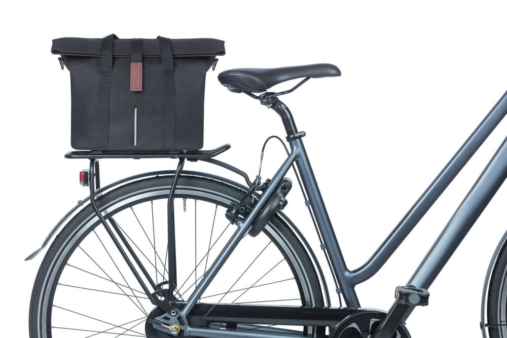 Schwarze Basil City MIK 2.0-KF-Hook Fahrrad-Handtasche mit Reflektor auf dunkelgrauem Gepäckträger.
